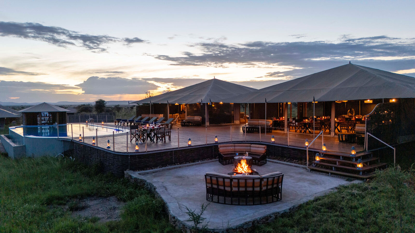 Campfire lit on the stone fire deck in front of the main tents at dusk, Arukore Simba Camp