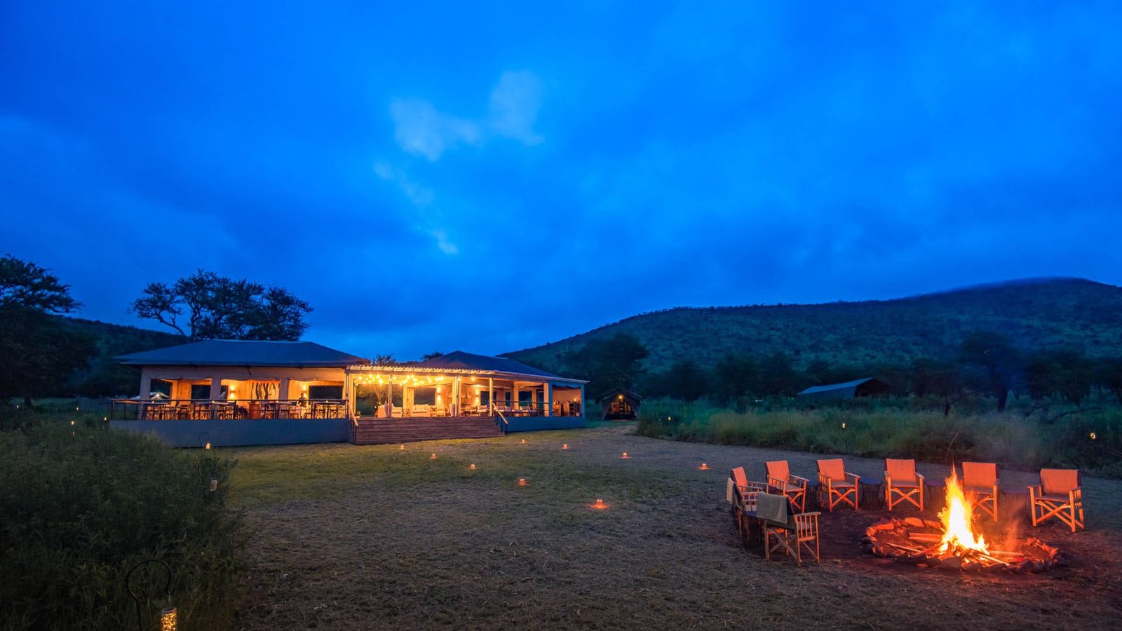 Dunia Camp mess tent lit at dusk with chairs around a campfire