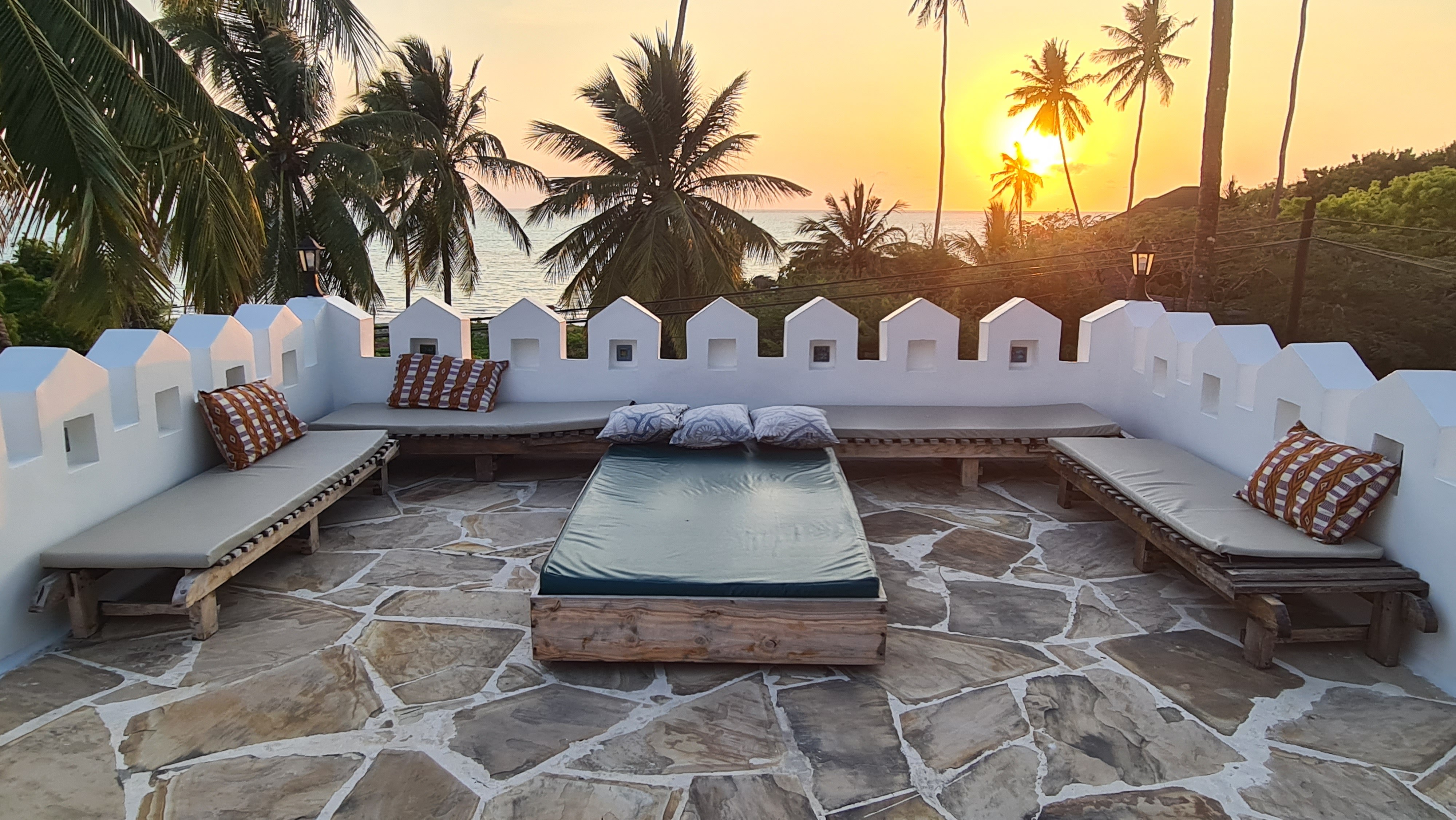 Rooftop day bed and cushioned benches at Kholle Villa with palms against the sunset