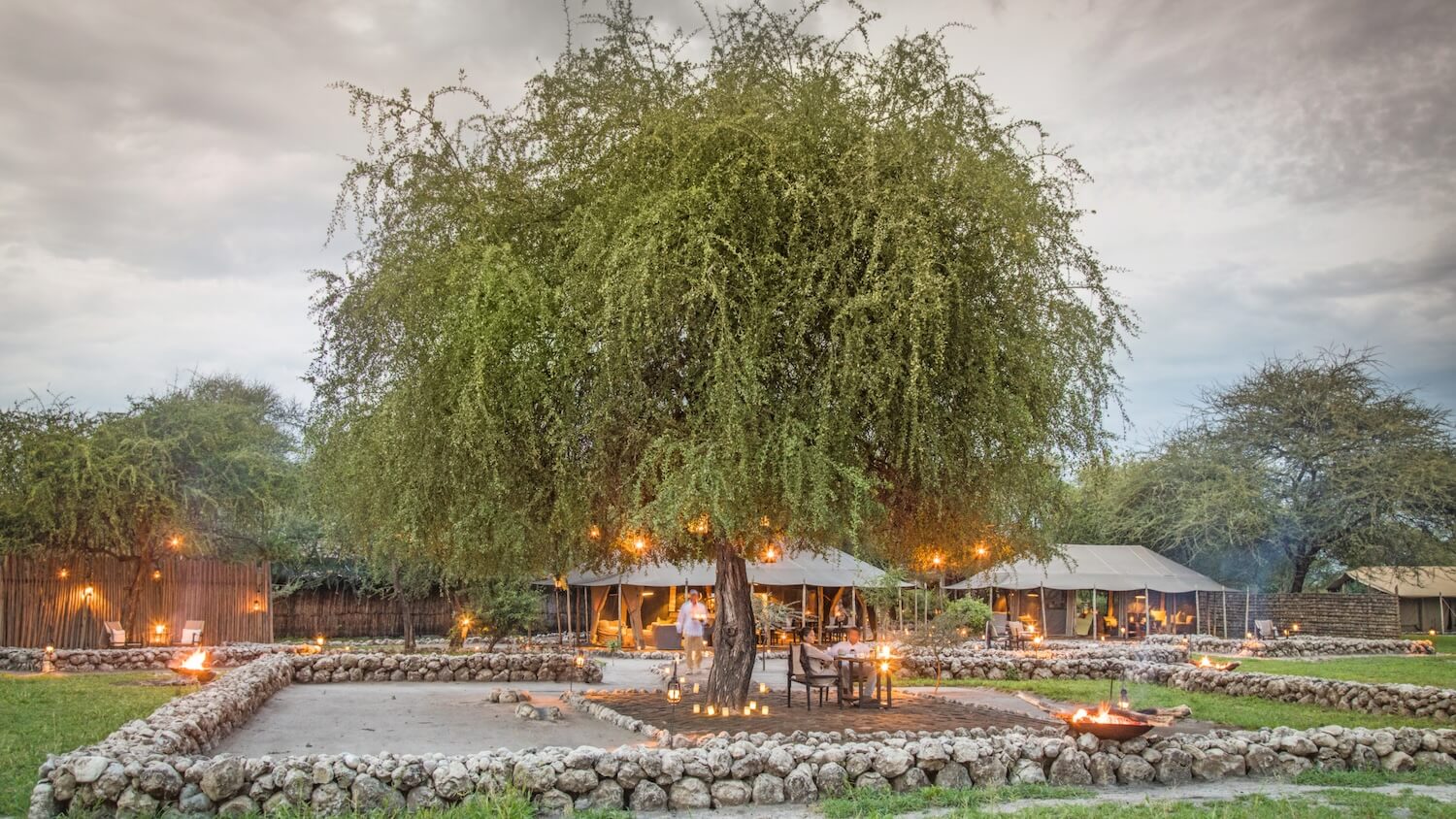 Little Chem Chem at dusk, the stone-ringed boma and lantern-lit tents beneath a large tree