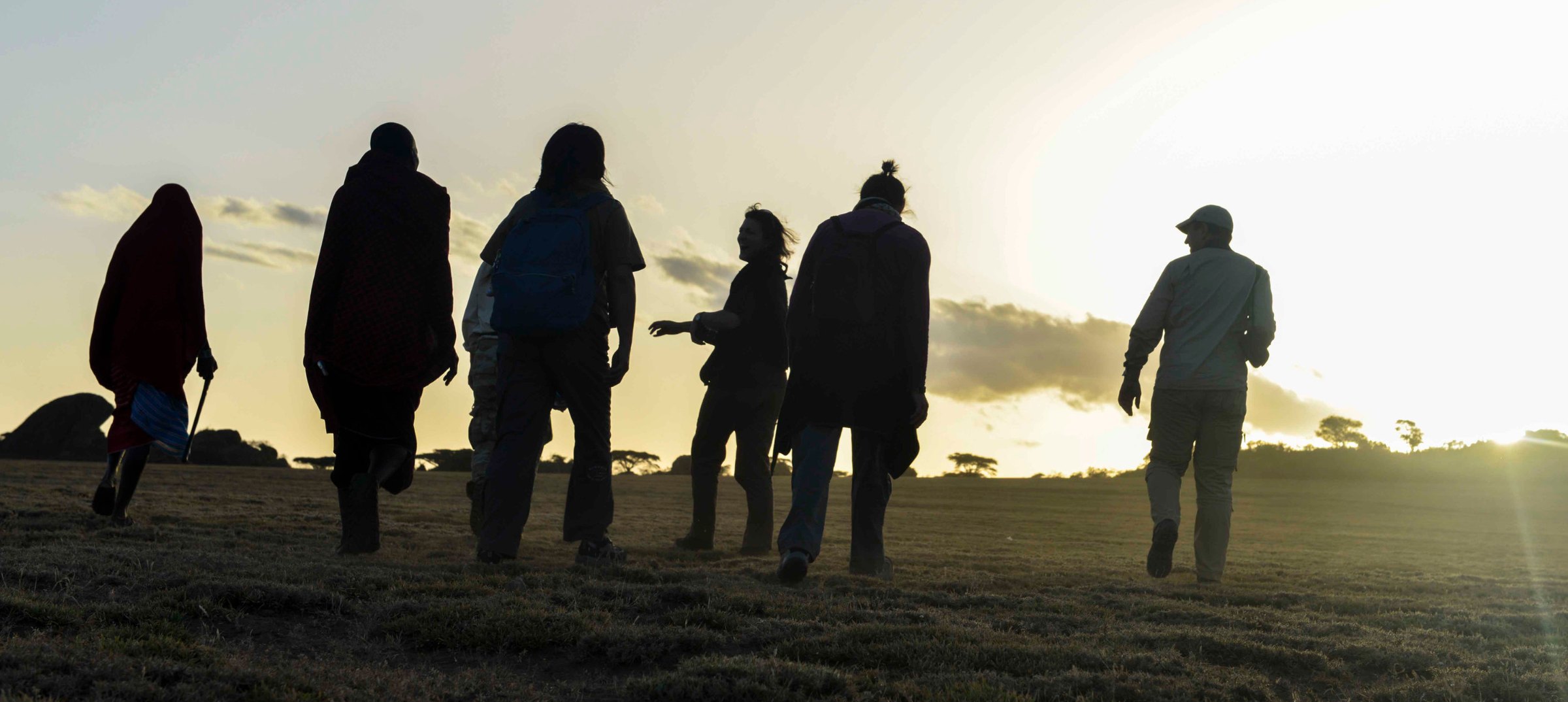 Guests and Maasai guides walking in silhouette across the plain at first light near Olduvai Camp