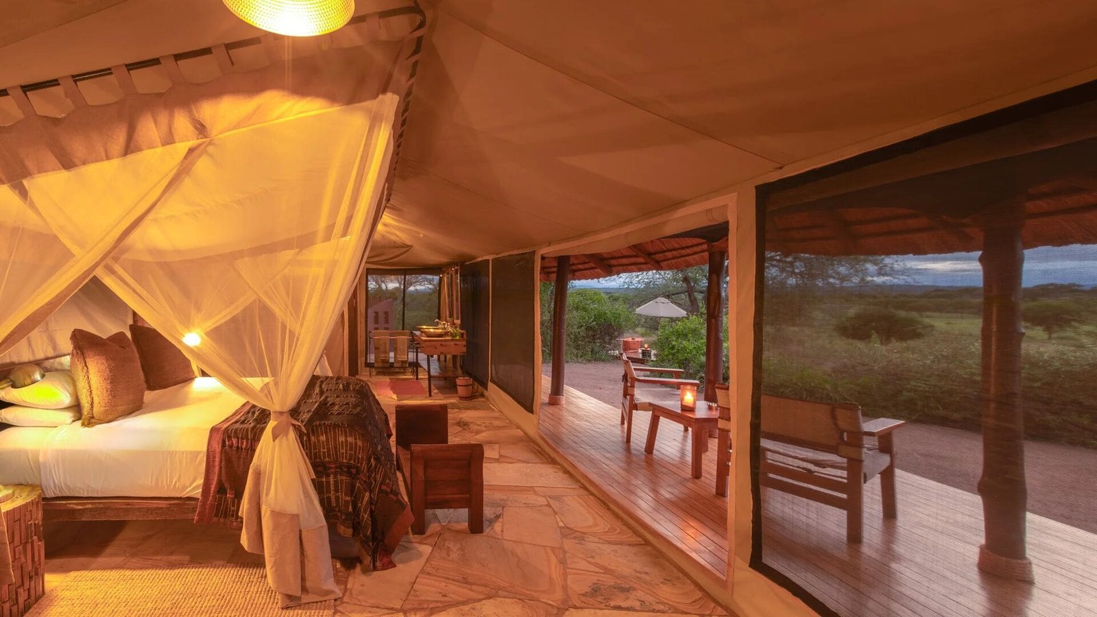Guest tent interior with mosquito net over the bed and doors opening onto a deck