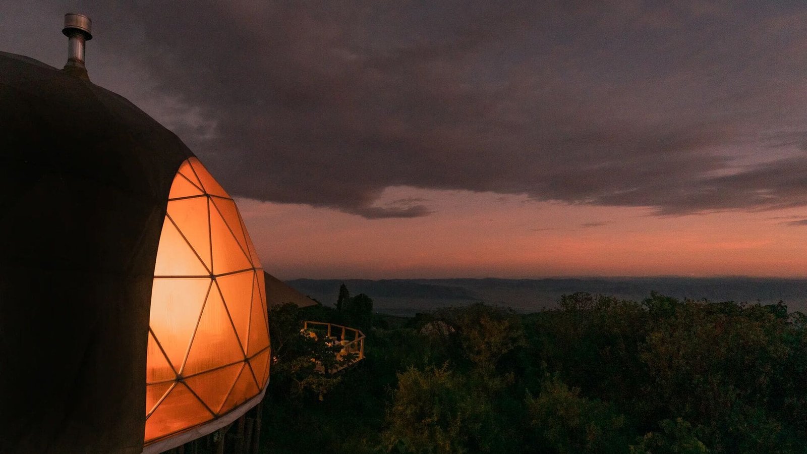 A lit geodesic dome at The Highlands at dusk above forested slopes